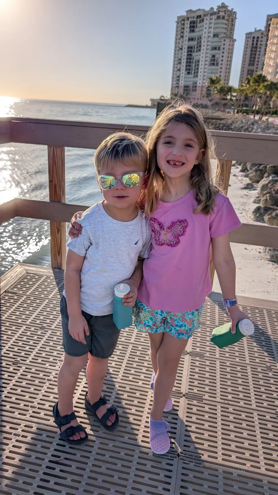 Abigail and Caleb side by side on a boardwalk by the water at sunset