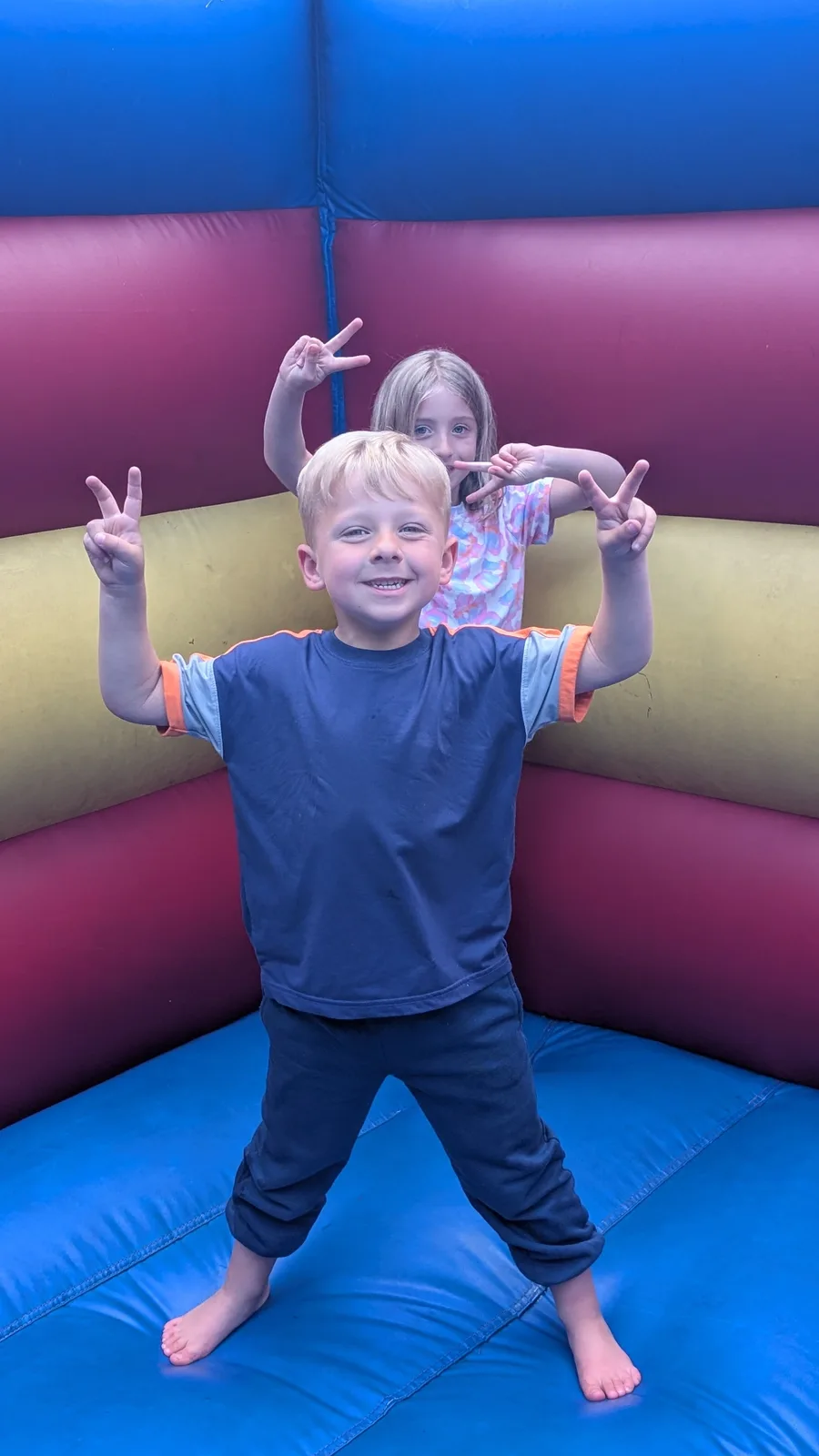 Caleb flashing peace signs in a bounce house, with Abigail behind him