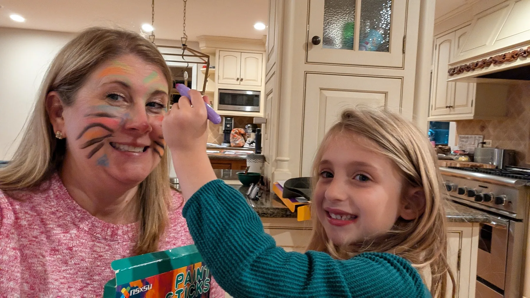 Abigail painting her mom's face at the kitchen counter