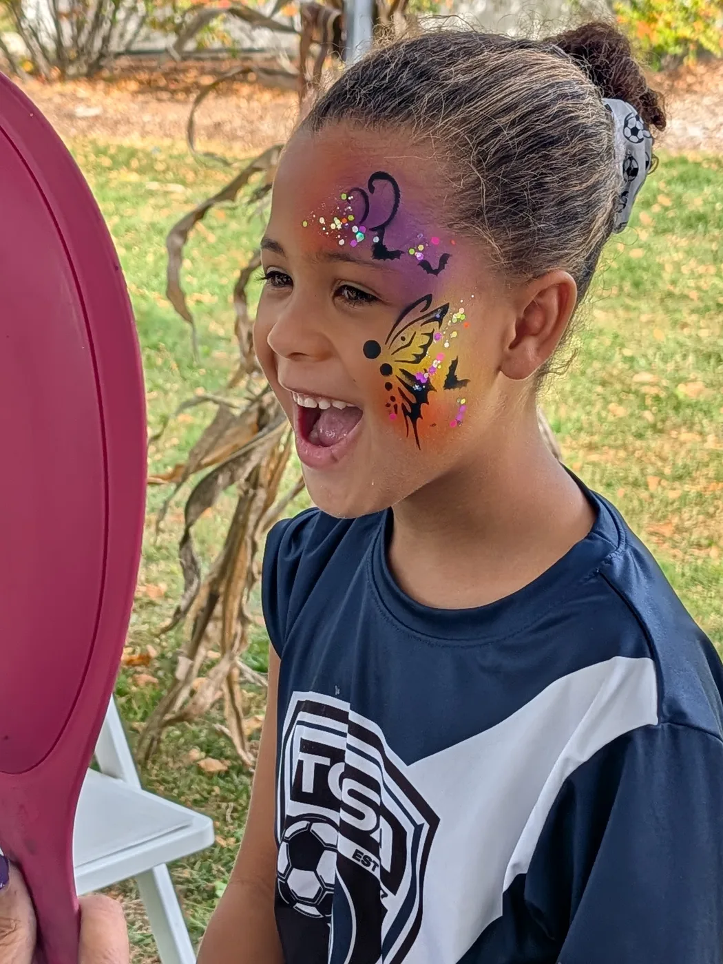 A child laughing while admiring a purple butterfly painted on her face