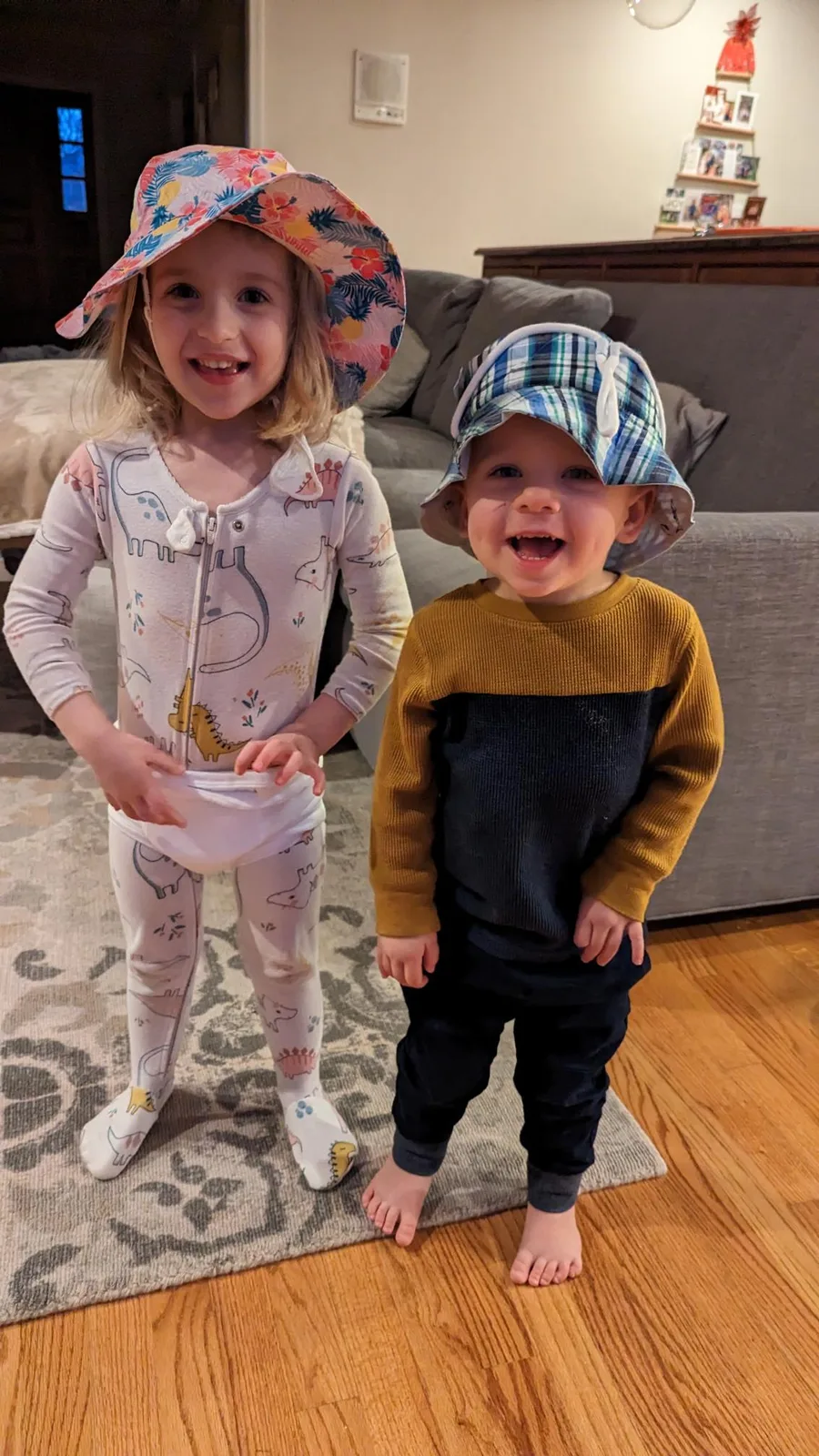 Abigail and Caleb in pajamas and floppy hats, grinning in the living room